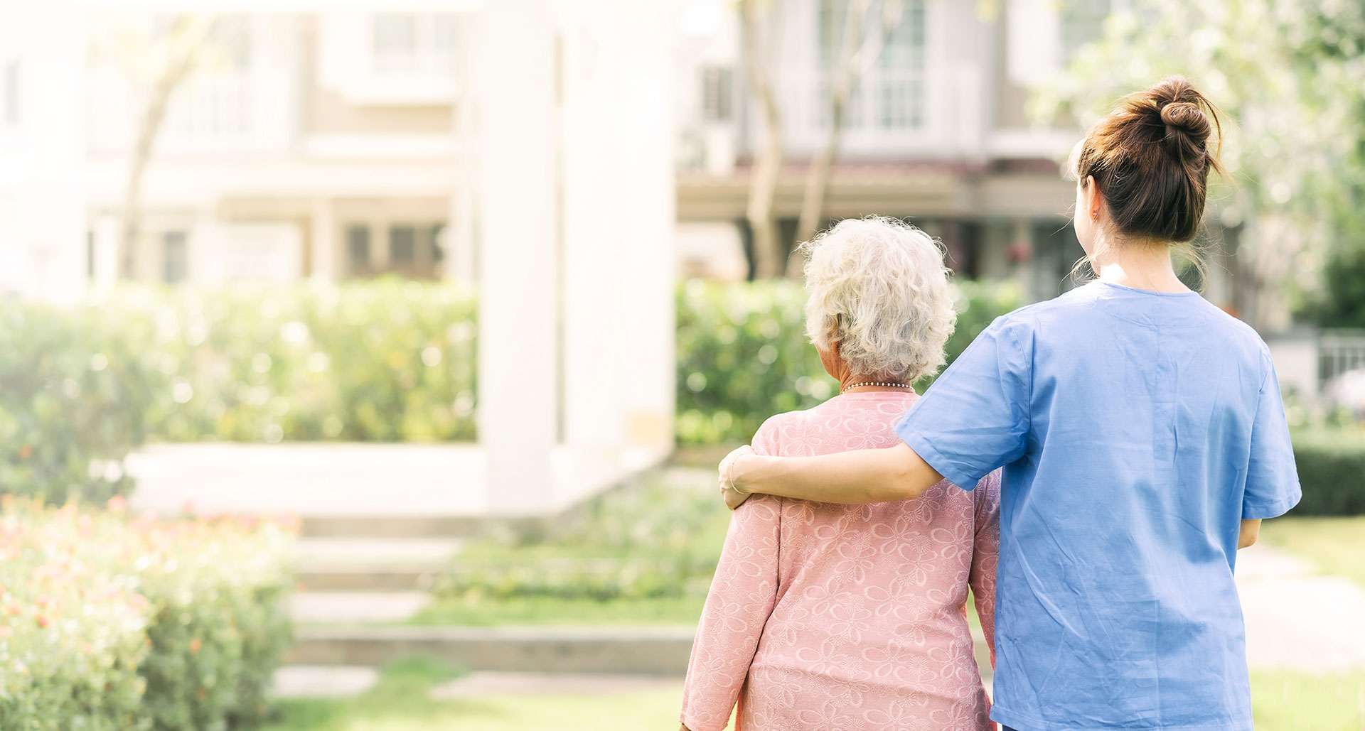 Une personnes âgée aidée par une aide soignante pour se promener dans le jardin d'une résidence, maison de retraite, EHPAD en région PACA de JCM Santé